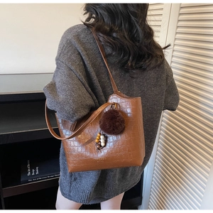 Detail of brown crocodile pattern tote bag with pompom charm on a female model