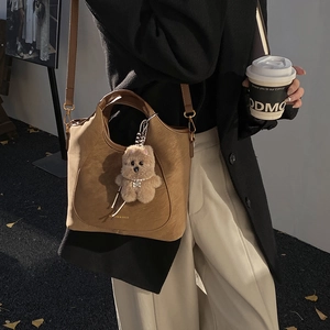 Detail of brown leather bucket bag featuring gold letters and plush bear charm