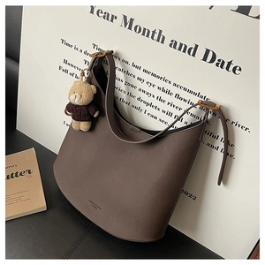 Détail du sac demi-lune en cuir marron foncé avec accessoire de charme ours en peluche