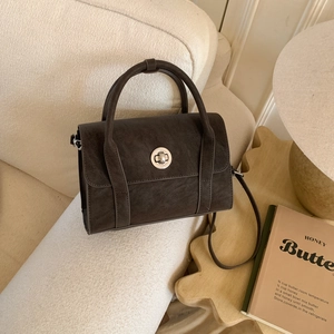 Close-up of retro dark brown crossbody bag with metal twist lock and matte texture