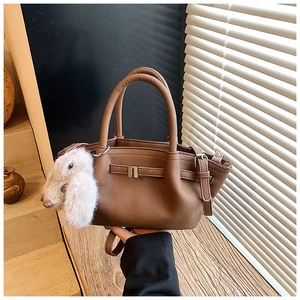 Detail view of brown pebbled leather bucket bag with a cute white plush bunny charm