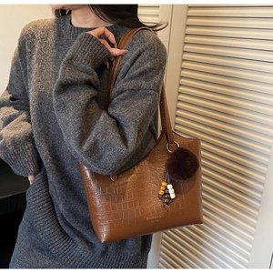 Close-up of brown crocodile pattern leather bucket bag with fur pompom and bead charm