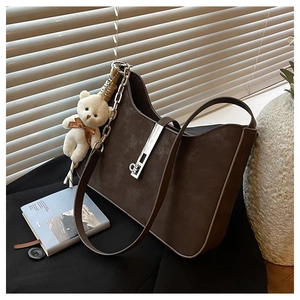 Detail of dark brown suede shoulder bag with silver metal lock and plush bear charm