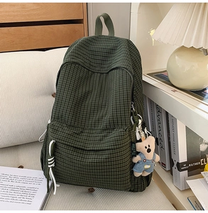 Detail of dark green checkered backpack with plush bear charm in cozy home setting