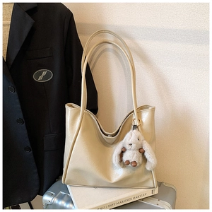 Detail view of a beige leather tote bag with a plush rabbit charm on a silver suitcase