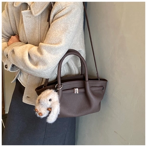 Detail of dark brown leather bucket bag with litchi texture and a cute rabbit charm