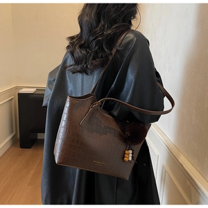 Detail of a brown crocodile embossed tote bag with gold lettering and plush charm