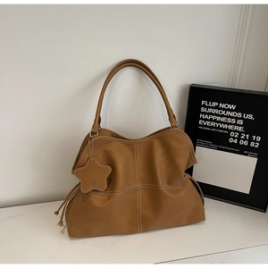 Detail of brown leather tote bag with white cross-stitching and a star-shaped pendant