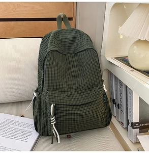 Detail view of green plaid backpack with white woven zipper pulls on a sofa