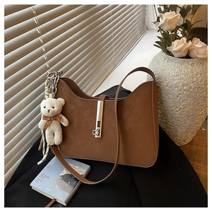 Detailed texture of brown suede shoulder bag with metal buckle and teddy bear charm