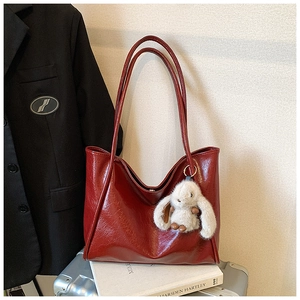 Detail of burgundy soft leather tote bag with a white plush bunny charm on a suitcase