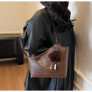 Detail of crocodile embossed dark brown tote bag with decorative fur ball on a model
