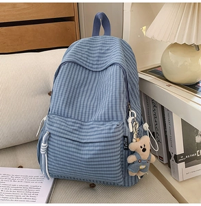 Detail of blue plaid canvas backpack featuring a large zipper pocket and cute plush bear charm