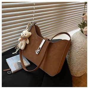 Brown suede shoulder bag with silver buckle and white bear charm in artistic lighting