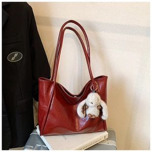 Detail of burgundy soft faux leather tote bag with cute plush rabbit charm on a suitcase