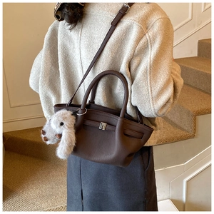 Detail of dark brown leather bucket bag with silver lock and white puppy plush charm