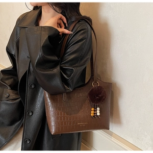 Detail of dark brown crocodile-textured bucket bag with gold logo and plush charm