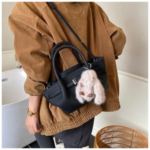 Detail of black leather bucket bag with silver clasp and plush rabbit pendant charm