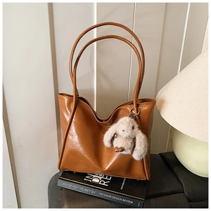 Detail of a large brown soft leather tote bag featuring a cute plush bunny charm