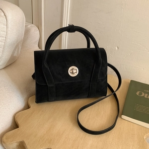Vintage black matte crossbody bag with silver lock on a wooden table in a cozy home setting
