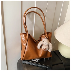 Detail view of caramel brown soft leather tote bag with cute rabbit plush keychain accessory
