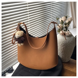 Détail d'un sac cabas en cuir marron caramel avec un ours en peluche sur un blazer noir
