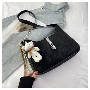 Detail of black suede shoulder bag featuring silver buckle and cute plush bear charm