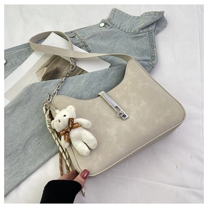 Detail of off-white shoulder bag with silver buckle and plush bear charm on denim background
