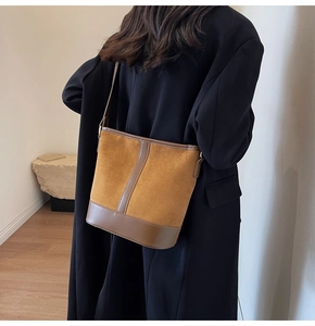 Detail of brown suede bucket bag texture paired with leather on model black coat