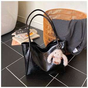 Detail of black large tote bag with glossy leather texture and cute plush rabbit charm