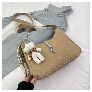 Detail of camel suede shoulder bag featuring a plush bear charm and woven rope accents