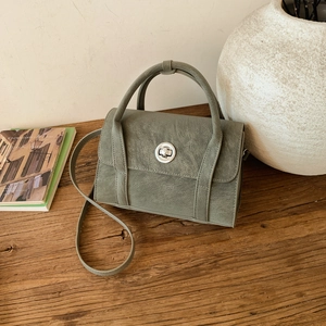 Detail of sage green vintage crossbody bag with silver twist lock on wooden desk