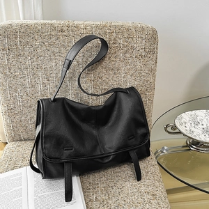Detail of a large black leather messenger bag featuring matte finish on a beige sofa