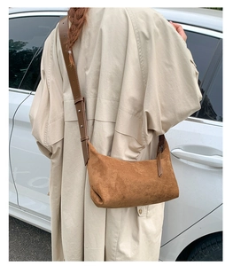 Close-up of brown suede crossbody bag with wide strap on a cream trench coat