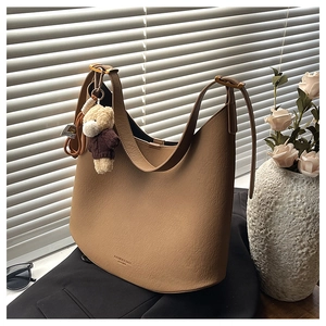 Détail du sac seau en cuir kaki avec charme d'ours en peluche et texture de grain