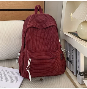 Detail shot of red plaid backpack with decorative rope knot and side pocket feature