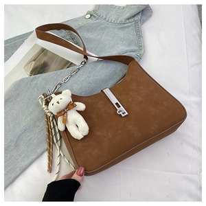 Detailed view of brown suede shoulder bag with retro buckle and plush bear pendant