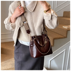 Detail of vintage brown bucket bag featuring wide woven strap and gold metal hardware accents