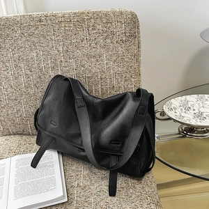 Detail of the black leather shoulder bag showing the wide strap and decorative side ties