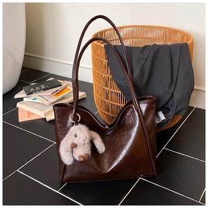 Detail of soft leather tote bag in dark coffee with a plush bunny charm and retro texture