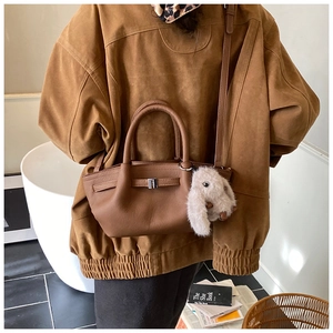 Brown lychee leather bucket bag with plush bunny charm shown in a lifestyle street shot