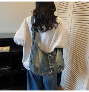 Detail of washed denim hobo bag with metal studs and adjustable strap on a model