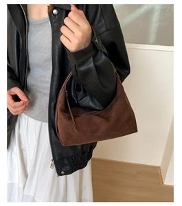 Close-up of a brown suede hobo bag styled with a leather jacket and white dress