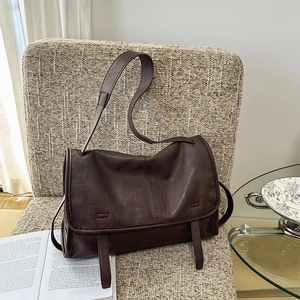 Detailed view of deep brown vintage leather messenger bag on a cozy fabric chair