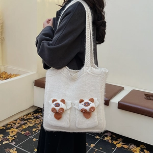 Close-up of a white knit tote bag featuring cute plush cat dolls and thick woven texture