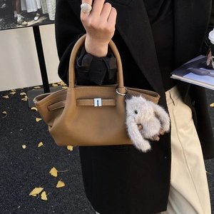 Close-up of brown pebbled leather bucket bag with silver buckle and plush rabbit charm