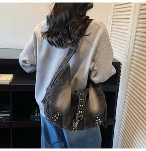 Close-up of washed denim hobo bag featuring silver punk rivets and metal buckle detail