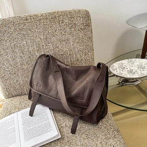 Close-up of vintage brown leather crossbody bag with wide strap on a woven chair