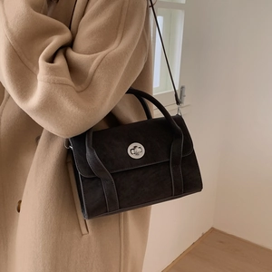 Detail of dark rectangle crossbody bag with silver ring lock on winter wool coat
