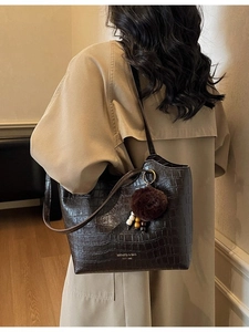 Retro dark brown croc-textured bucket bag with plush charm shown on a chic trench coat